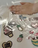 Mão alisando o filme hotfix transparente sobre apliques bordados numa blusa branca
