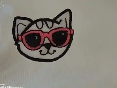 Aplique bordado de gato de óculos numa blusa branca, durante a aplicação do filme hotfix